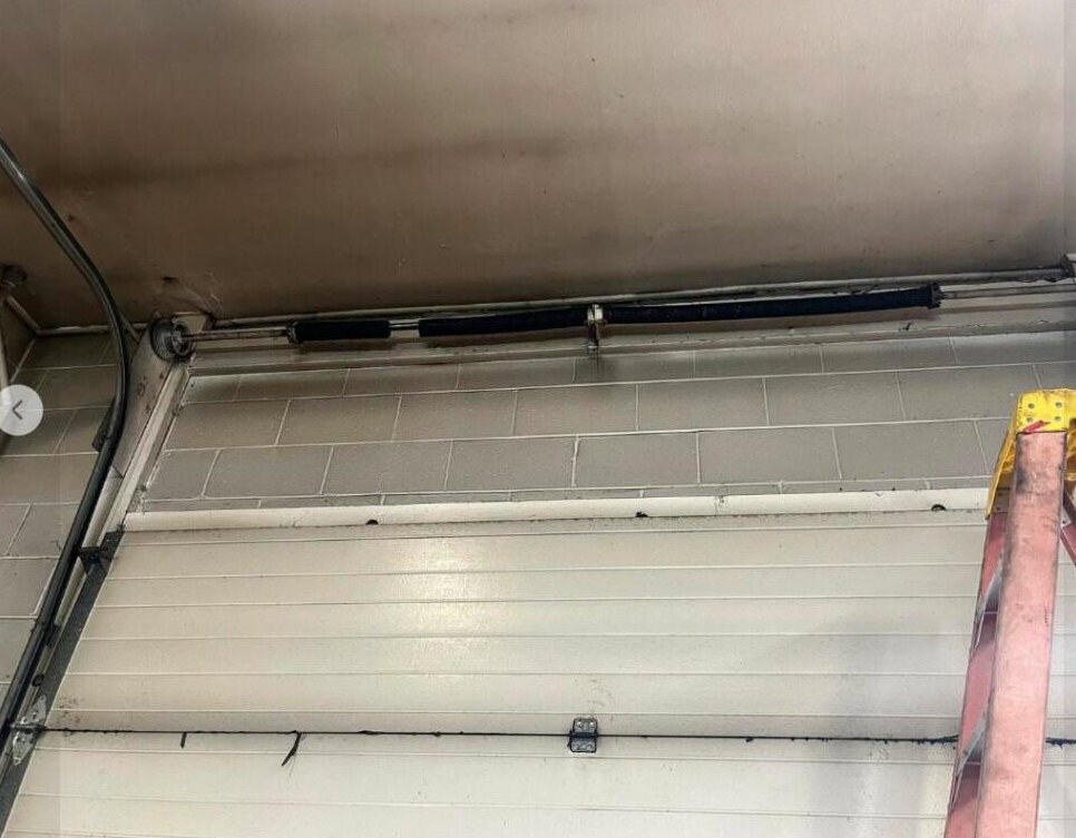 Technician replacing a garage door spring on a ladder